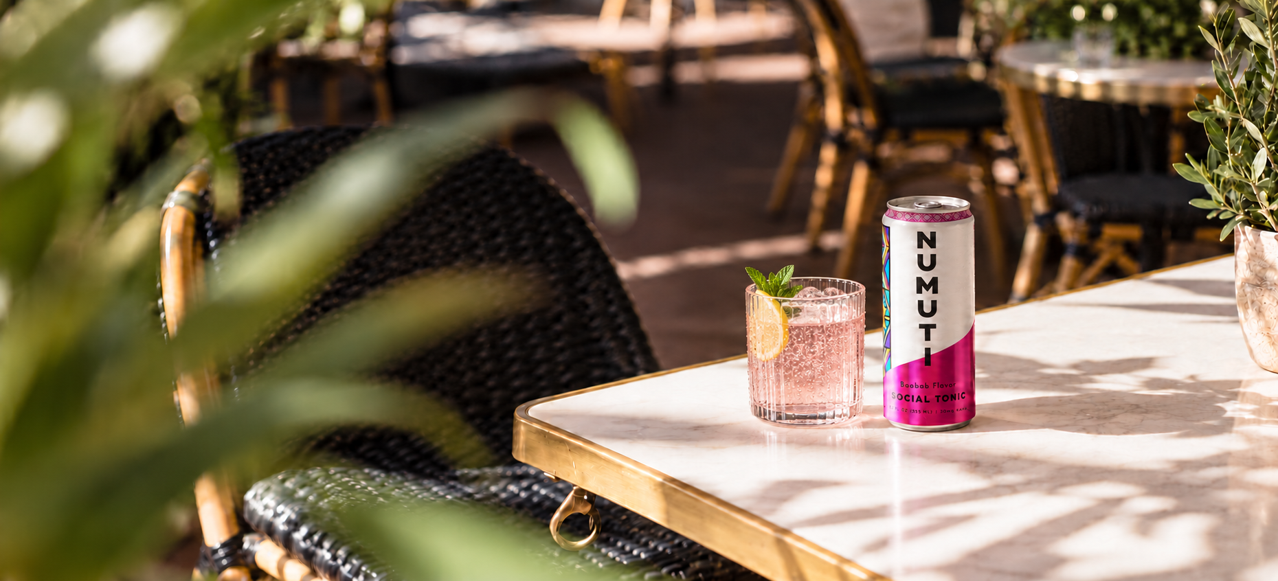 Numuti Baobab can and a pale pink drink on a sunlit café table