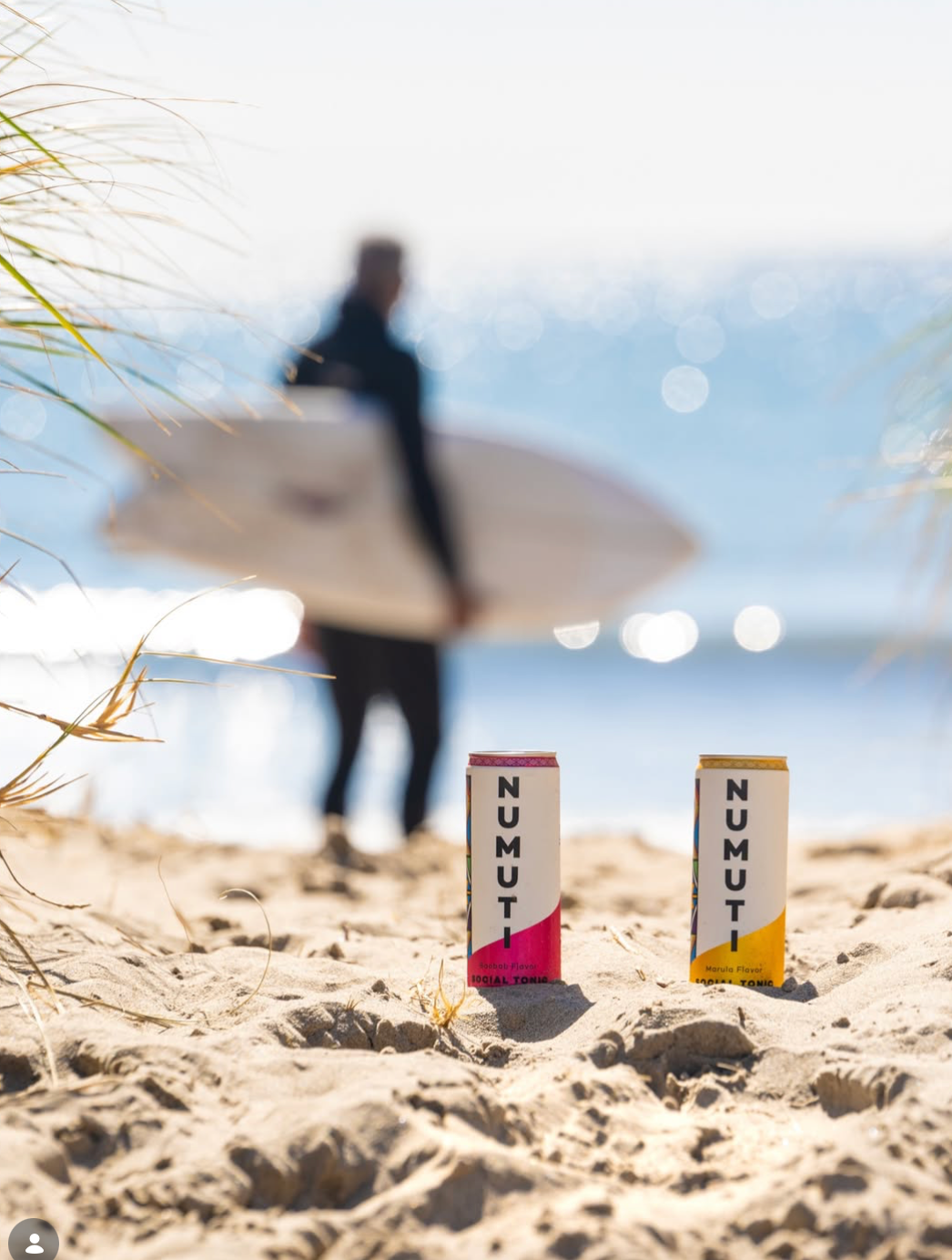 NuMuti cans on the beach with a surfer